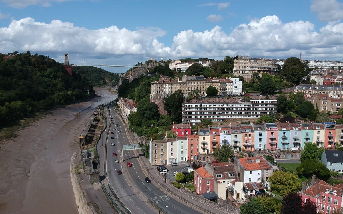 Drone view of pastel-painted terraced houses beside the River Avon in Bristol, with Clifton Suspension Bridge behind