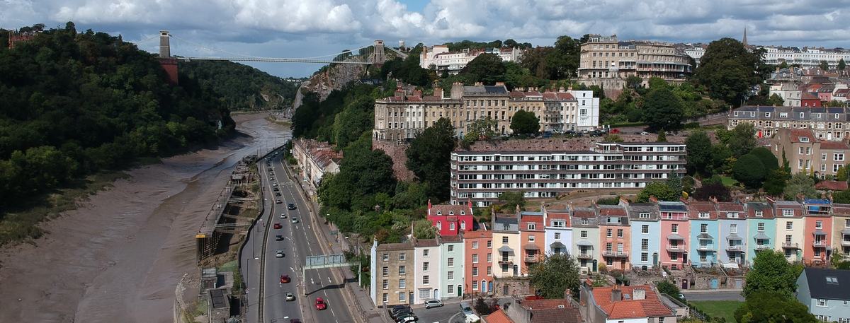 Drone view of pastel-painted terraced houses beside the River Avon in Bristol, with Clifton Suspension Bridge behind