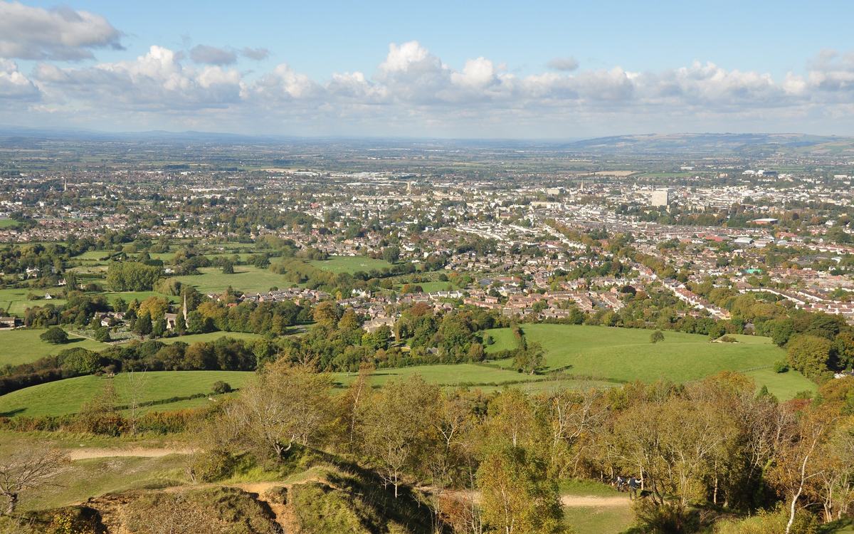 View over Cheltenham from Leckhampton Hill, with green fields and trees in front and the town spreading to the horizon