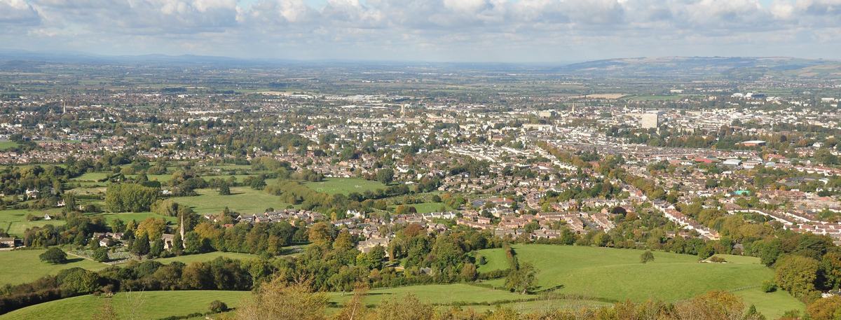 View over Cheltenham from Leckhampton Hill, with green fields and trees in front and the town spreading to the horizon