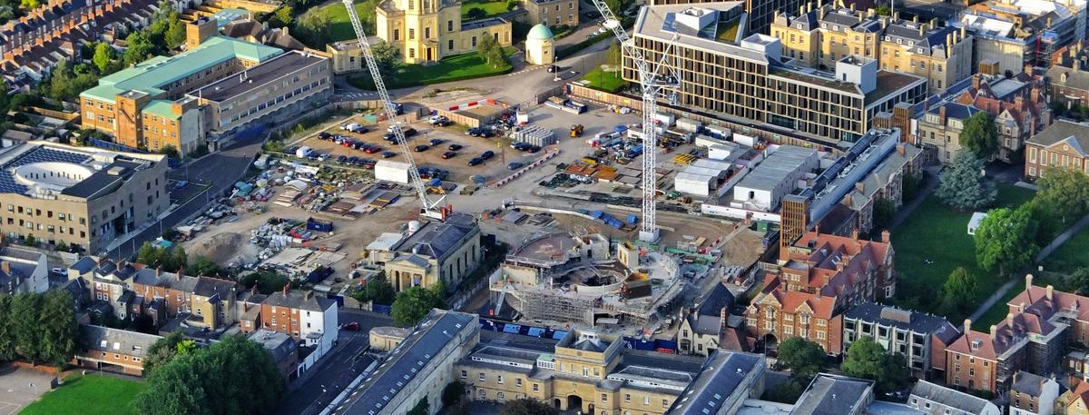 Aerial view of a construction site in Oxford with two tower cranes and a circular building under construction