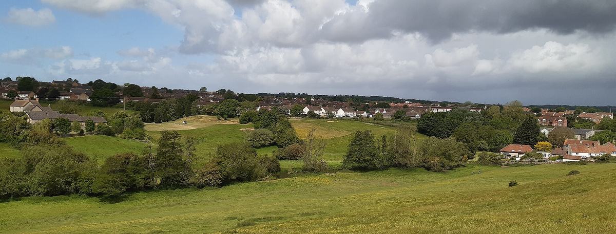 View from a hillside across the River Chew valley towards the houses of Keynsham under a partly cloudy sky