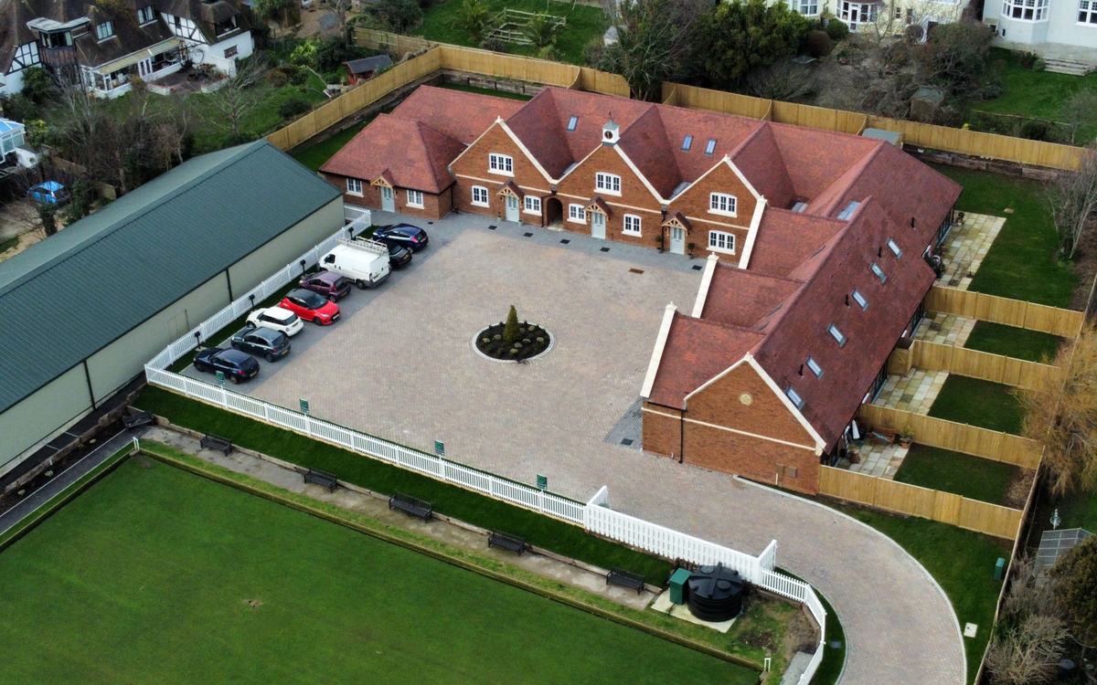 Drone view of a small new-build development of red-brick houses with tiled roofs, private gardens and a paved courtyard