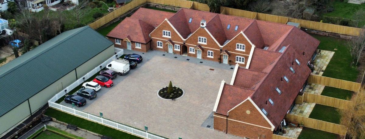 Drone view of a small new-build development of red-brick houses with tiled roofs, private gardens and a paved courtyard