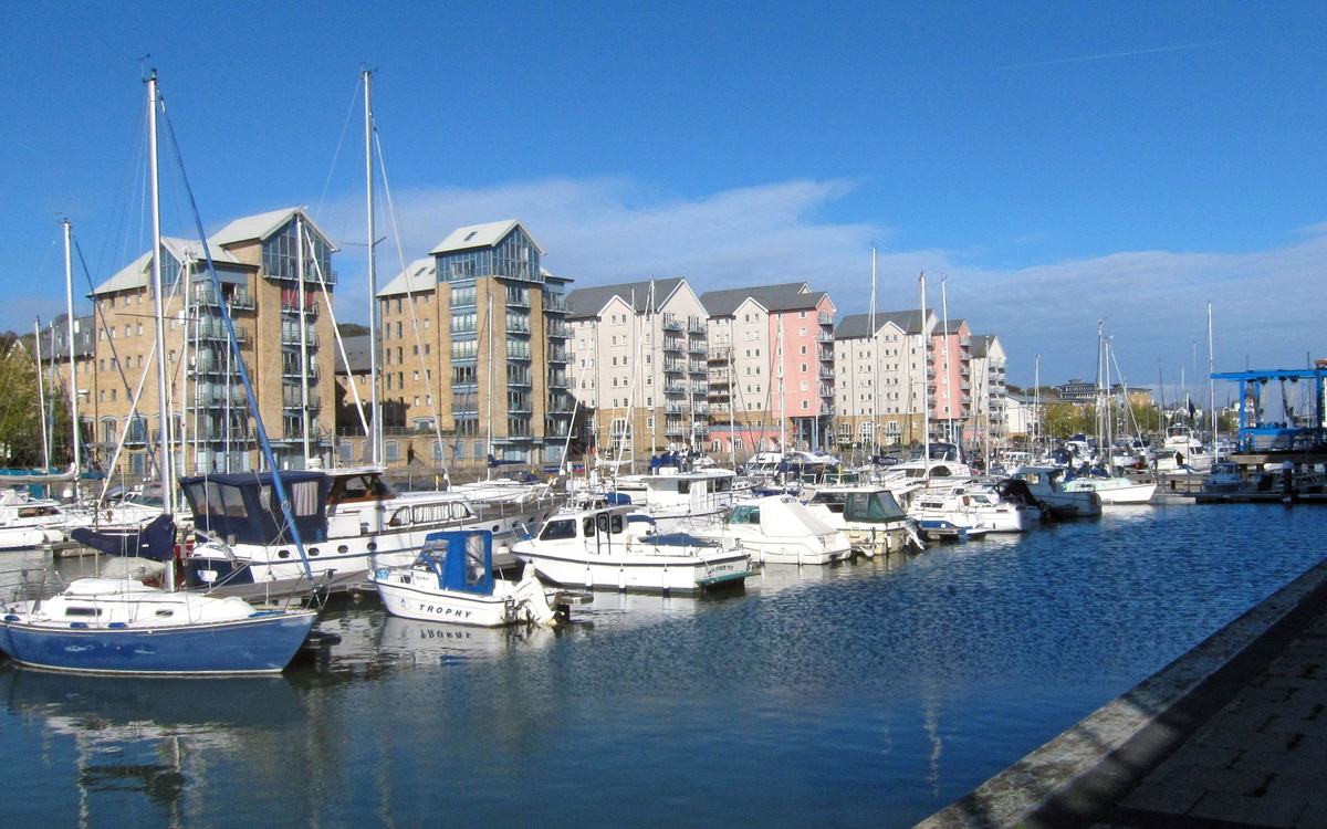 Yachts and motor boats moored in Portishead Marina in front of colourful waterside apartments under a blue sky