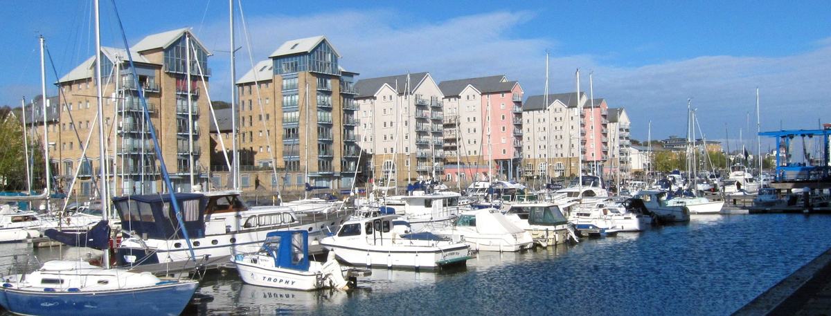 Yachts and motor boats moored in Portishead Marina in front of colourful waterside apartments under a blue sky
