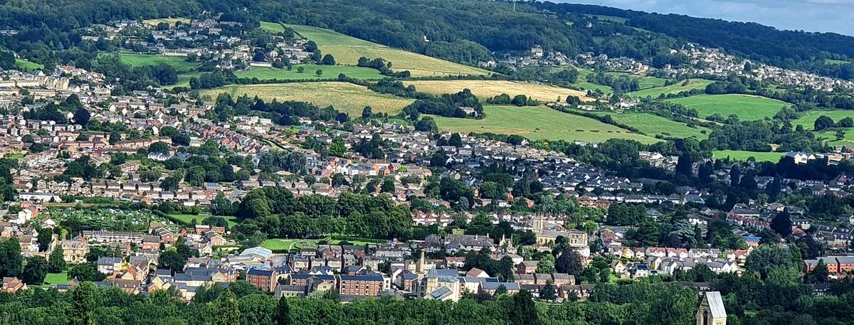 View from Selsley Common towards Stroud: houses across the valley and hillsides, green fields and a village church