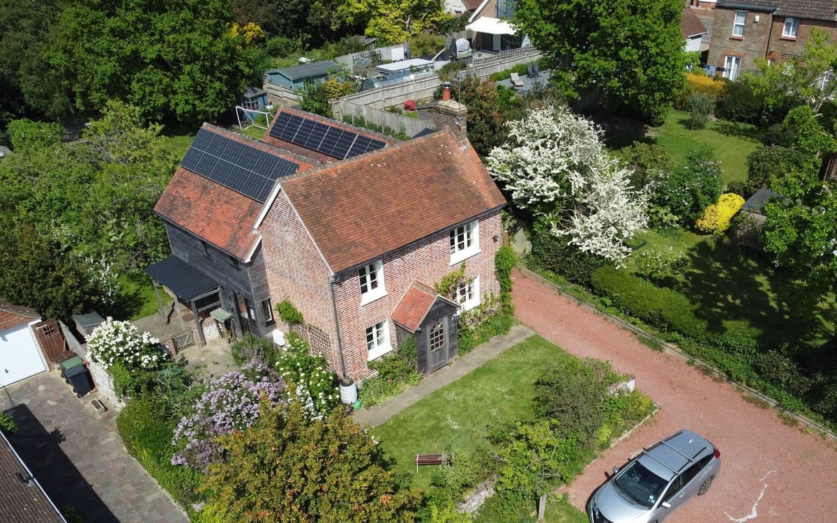 Drone view of a red-brick cottage with clay-tiled pitched roofs, a brick chimney and rooftop solar panels