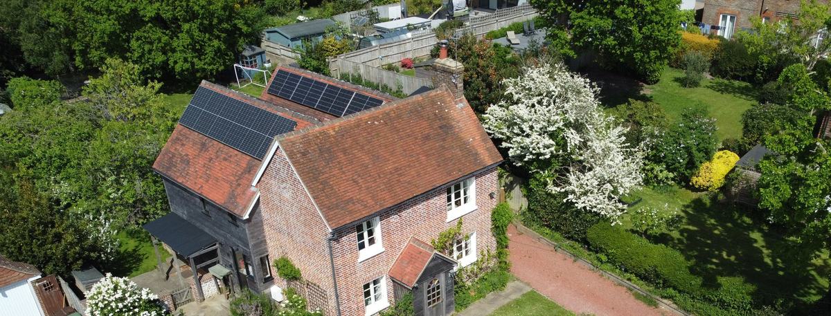 Drone view of a red-brick cottage with clay-tiled pitched roofs, a brick chimney and rooftop solar panels