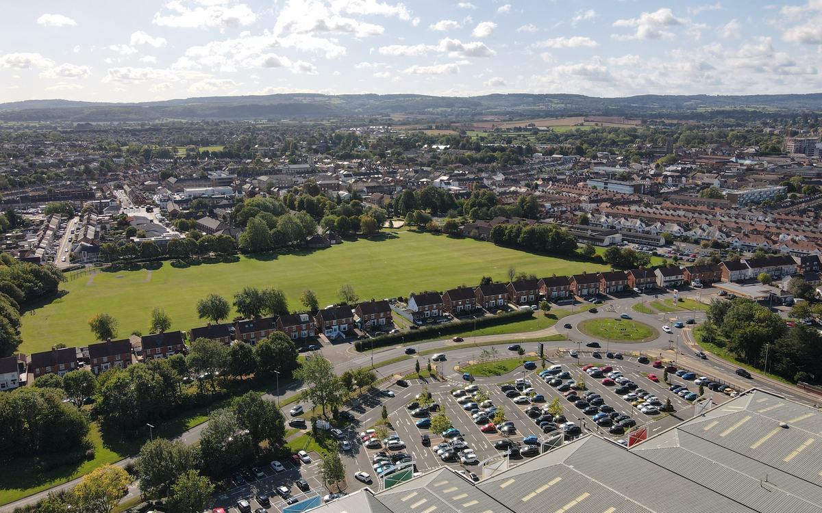 Drone view over Victoria Park in Taunton, with surrounding streets and wooded hills on the horizon under a blue sky